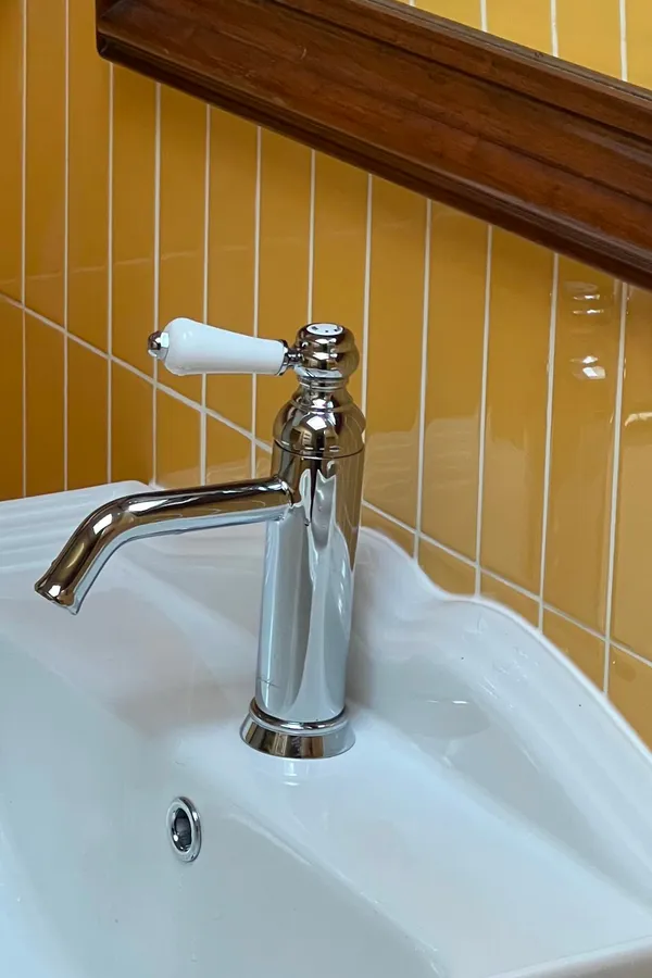 Robinetterie rétro chromée sur lavabo blanc et carrelage jaune moutarde pour une salle de bain à Concarneau