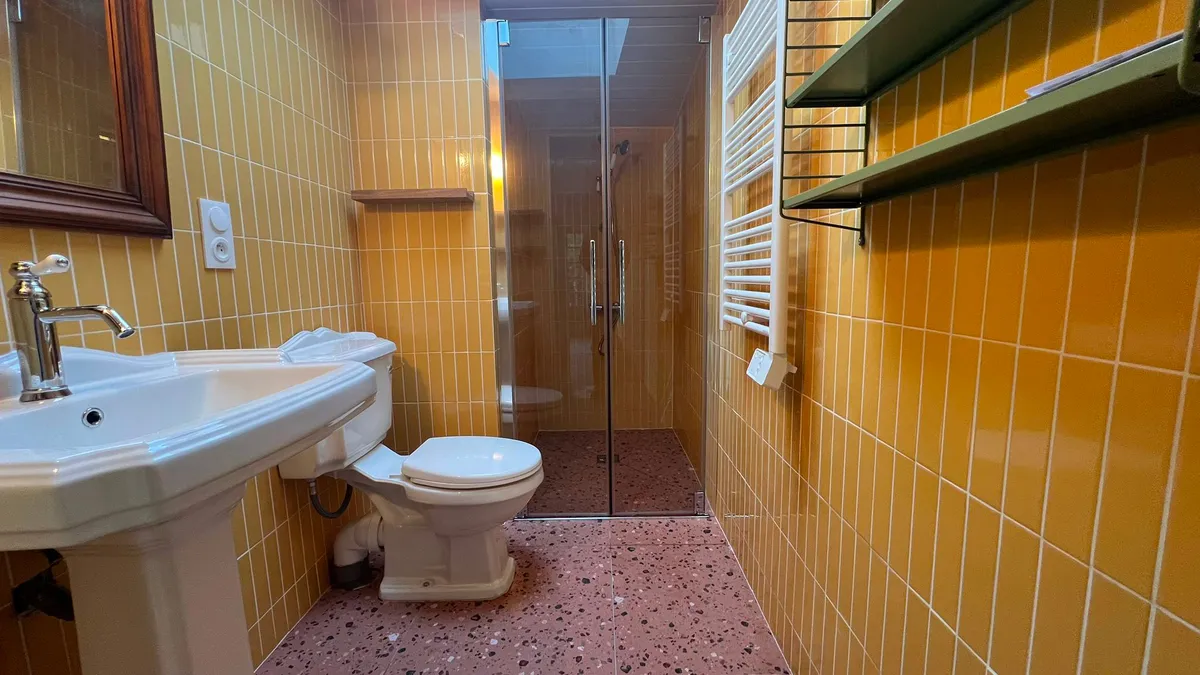 Rénovation de salle de bain à Concarneau avec carrelage jaune moutarde, sol en terrazzo et robinetterie rétro